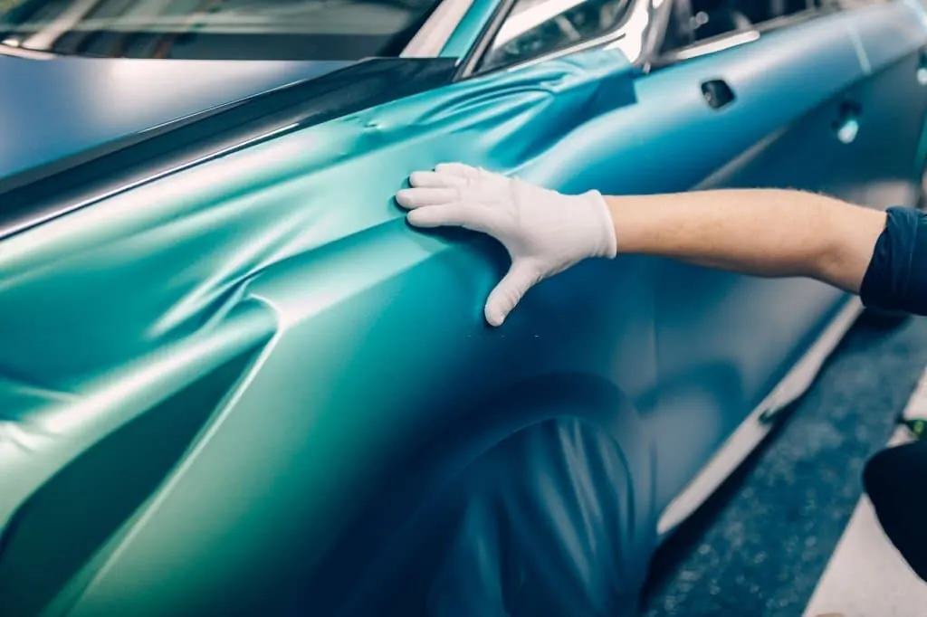 Gloved hand pressing satin teal vinyl wrap into a body line