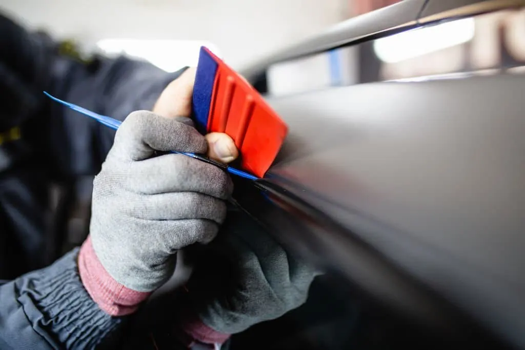 Gloved hand running a felt squeegee over vinyl on a body panel